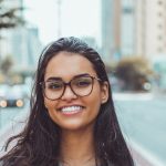 A young woman with glasses smiling on a city street, embracing urban lifestyle.