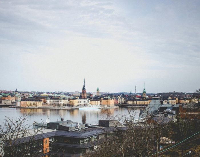 Aerial view of Stockholm's historic skyline reflecting across the river under a cloudy sky.